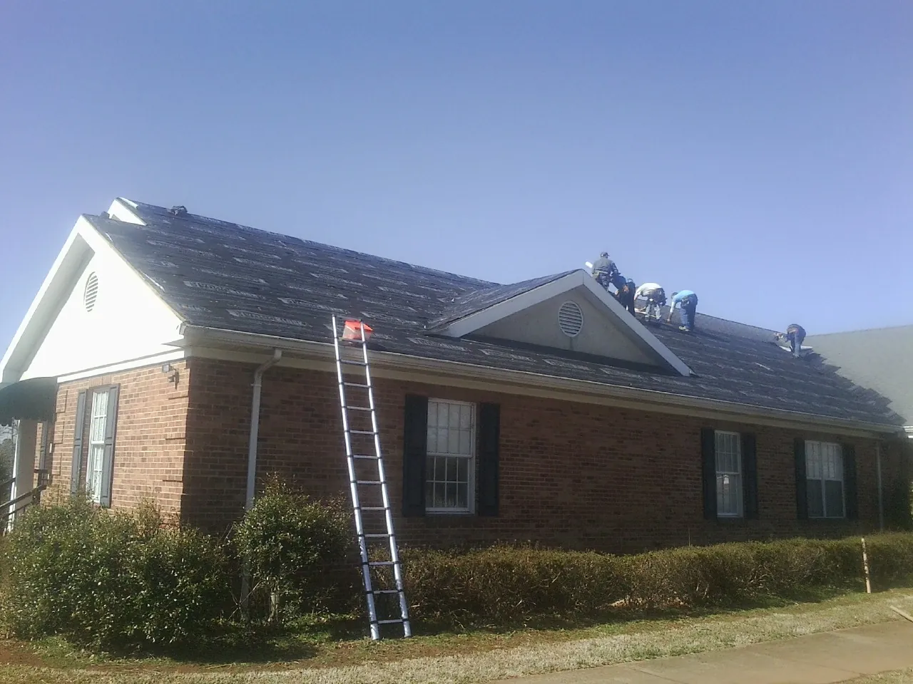 Crew tearing shingles off a brick ranch roof with a ladder set — Metal Roof Repair work by our crew in Wellesley Hills