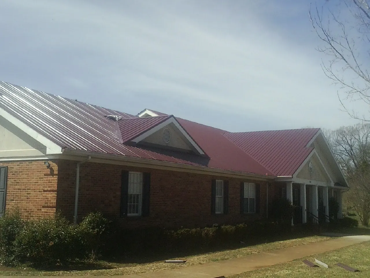 Red metal roof with gabled entries on a long brick building, from a Hail Damage Roof Repair job in Wellesley Hills