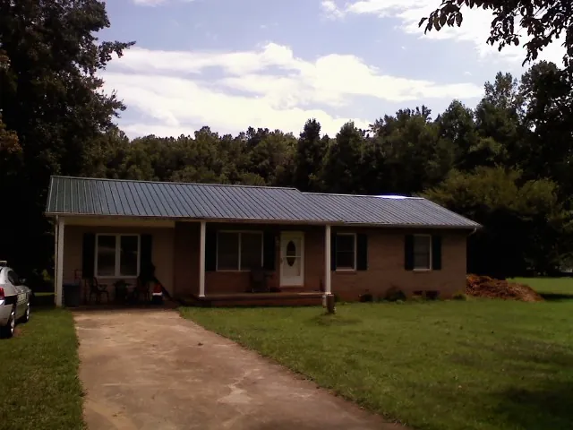 Dark green metal roof on a brick ranch with a covered porch in Wellesley Hills