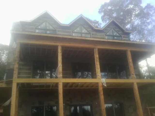 Dormers and porch framing on a large log home under construction — Roof Coating work by our crew in Wellesley Hills