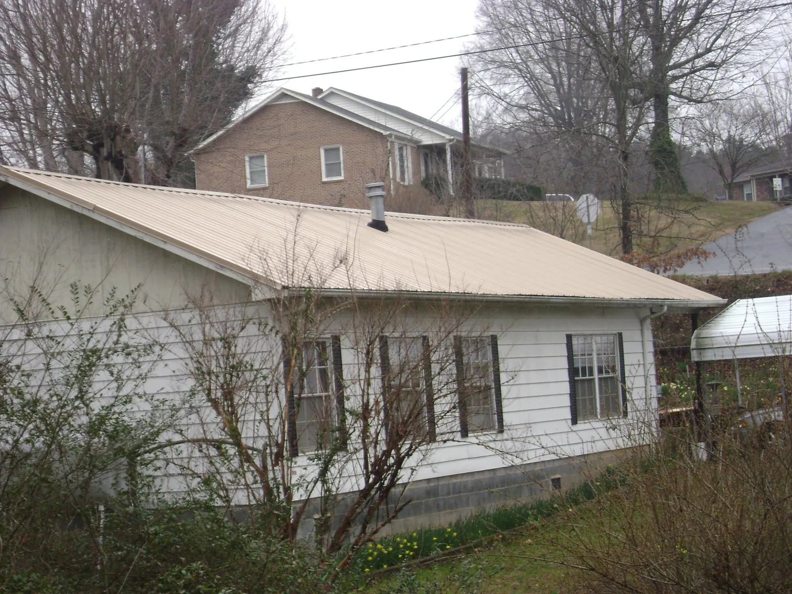 Tan metal roof on a white sided house set into a hillside — Commercial Roofing by Roofing Brothers in Wellesley Hills