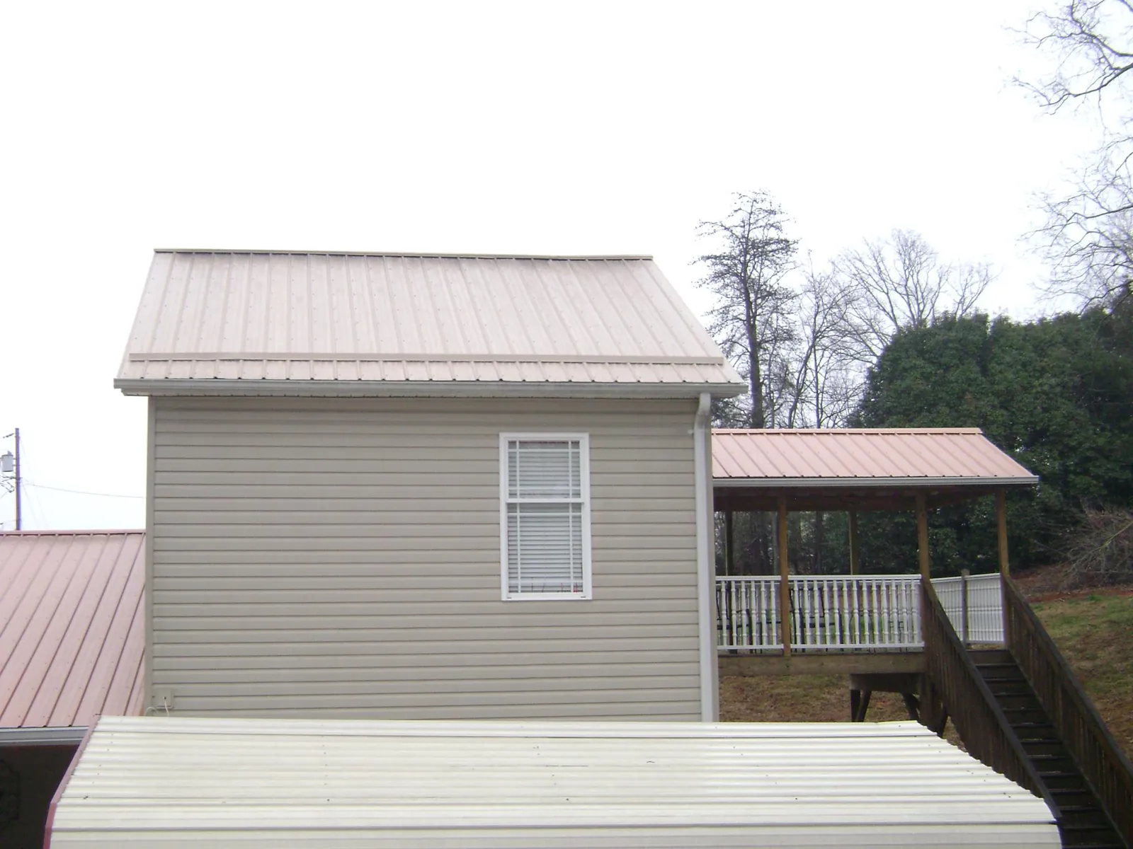 Tan metal roofs on a two story addition and attached porch, from a Roof Replacement job in Wellesley Hills
